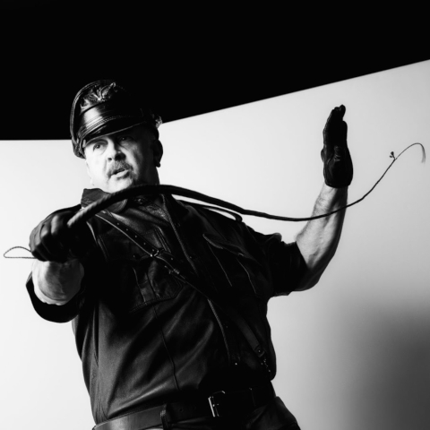 Cuir Nikolas in leather cap black shirt and gloves, snapping a singletail whip